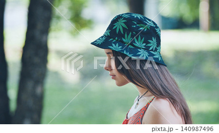 Teenage girl relaxing in park, sporting cannabis patterned bucket hat under sunny skies 140987496