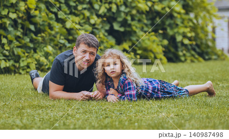 Father and daughter lying on grass, spending quality time together in the garden, enjoying a sunny family day 140987498