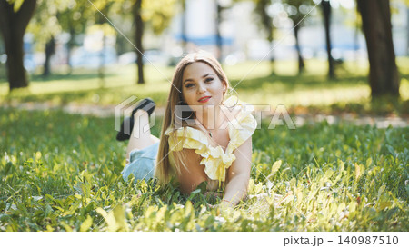 Relaxed female resting on verdant lawn, basking in golden sunlight and experiencing serene summer moment Relaxed female resting on verdant lawn, basking in golden sunlight and experiencing serene summer moment 140987510