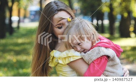 Young mother is holding and comforting her crying daughter in a park during a sunny autumn day Young mother is holding and comforting her crying daughter in a park during a sunny autumn day 140987527
