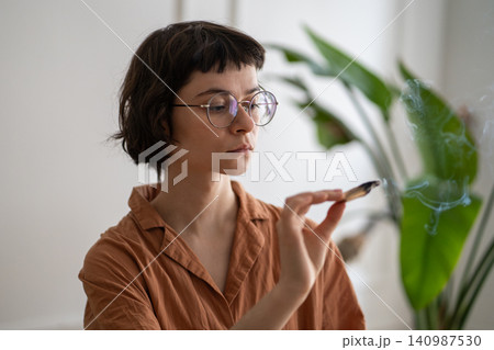Calm woman lighting up aromatic palo santo smudging stick at home for sensory therapy and meditation Calm woman lighting up aromatic palo santo smudging stick at home for sensory therapy and meditation 140987530