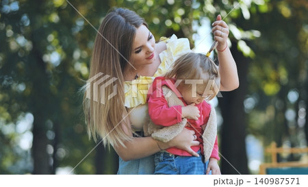Young mother gently fixing her shy daughter's hair in a park, enjoying a sunny autumn day filled with warmth and joy Young mother gently fixing her shy daughter's hair in a park, enjoying a sunny autumn day filled with warmth and joy 140987571