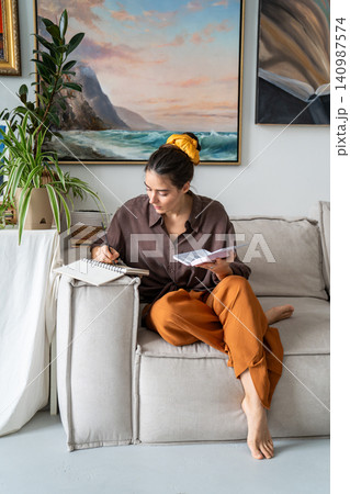 Relaxed woman painter enjoying art hobby therapy, drawing pictures with watercolor sitting on couch. 140987574