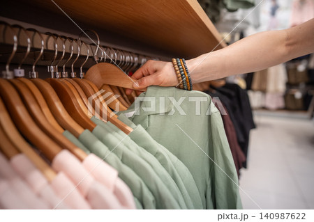Female customer taking colorful summer shirt from hanger display at popular clothing store. 140987622