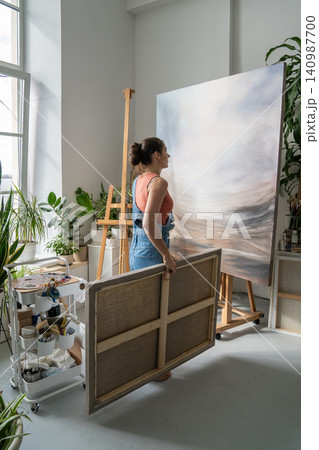 Talented focused woman painter artist working in home studio, looking at canvas painting on easel. Talented focused woman painter artist working in home studio, looking at canvas painting on easel. 140987700