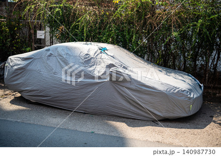 Car parked on street in Thailand covered with silver waterproof cover protection from intense heat. Car parked on street in Thailand covered with silver waterproof cover protection from intense heat. 140987730