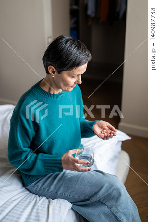 Unwell senior woman holding pills and glass of water, awareness of prevention illness at older age. Unwell senior woman holding pills and glass of water, awareness of prevention illness at older age. 140987738