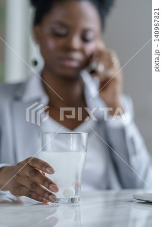 Black woman hold sparkling water glass with dissolving effervescent aspirin pill taking medication Black woman hold sparkling water glass with dissolving effervescent aspirin pill taking medication 140987821