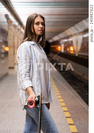 Woman with longboard wait for train at metro station. Female at underground platform with skate Woman with longboard wait for train at metro station. Female at underground platform with skate 140987822