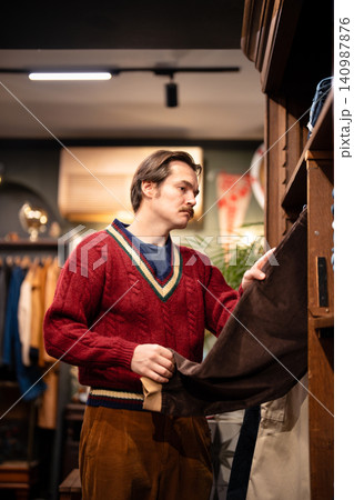 Handsome stylish guy choosing velvet jeans from display in fashionable vintage selective shop. 140987876