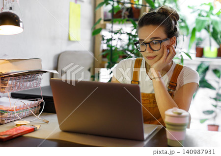 Female gardener in glasses working on laptop in home garden, freelance concept 140987931