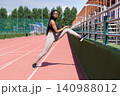 African American sportswoman stretches legs on jogging track preparing for running on sunny day 140988012
