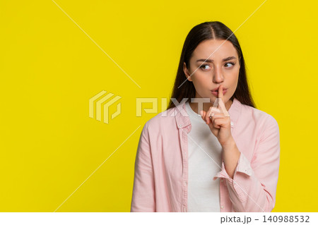 Woman placing finger on lips showing silence gesture asking for quiet serious thoughtful expression Woman placing finger on lips showing silence gesture asking for quiet serious thoughtful expression 140988532