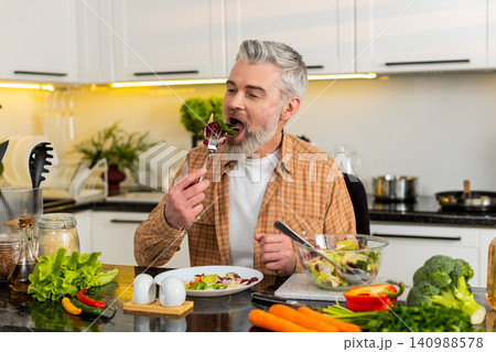Middle-aged man serving fresh vegetable salad on plate in home kitchen smiling for healthy diet meal Middle-aged man serving fresh vegetable salad on plate in home kitchen smiling for healthy diet meal 140988578