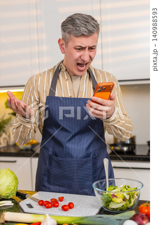 Middle-aged man reading bad smartphone message in kitchen feeling defeat failure and serious problem Middle-aged man reading bad smartphone message in kitchen feeling defeat failure and serious problem 140988593