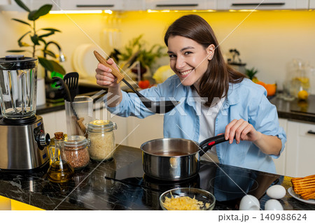 Young woman cooking homemade soup in modern kitchen stirring pot for healthy diet nutrition indoors Young woman cooking homemade soup in modern kitchen stirring pot for healthy diet nutrition indoors 140988624
