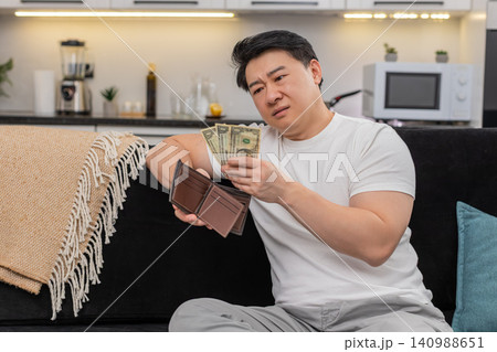 Asian man checks wallet sees only small dollar bills frowns and sets saving goal for budget plan new Asian man checks wallet sees only small dollar bills frowns and sets saving goal for budget plan new 140988651