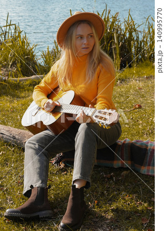 Portrait of smiling caucasian artist plays wooden acoustic guitar in autumnal park. Young songwriter plays string musical instrument hobby outside in nature fall time. Audio music healing Portrait of smiling caucasian artist plays wooden acoustic guitar in autumnal park. Young songwriter plays string musical instrument hobby outside in nature fall time. Audio music healing 140995770