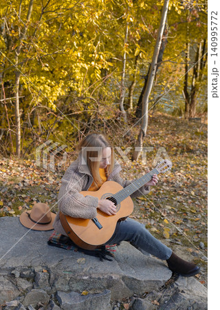 Portrait of smiling caucasian artist plays wooden acoustic guitar in autumnal park. Young songwriter plays string musical instrument hobby outside in nature fall time. Audio music healing 140995772