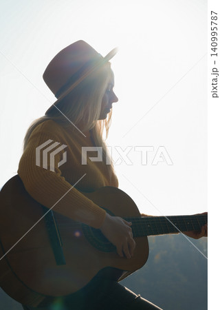 Portrait of smiling caucasian artist plays wooden acoustic guitar in autumnal park. Young songwriter plays string musical instrument hobby outside in nature fall time. Audio music healing Portrait of smiling caucasian artist plays wooden acoustic guitar in autumnal park. Young songwriter plays string musical instrument hobby outside in nature fall time. Audio music healing 140995787