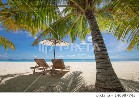 Sun loungers facing a calm turquoise lagoon. Palm trees and red umbrella on pristine sand. Luxury tropical resort for travel destination summer holiday 140997743