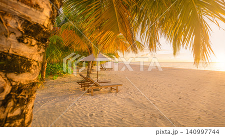 Golden sunset glowing over palm shaded beach loungers. Warm light spilling across a tropical shore. Romantic resort escape for luxury travel summer holiday Golden sunset glowing over palm shaded beach loungers. Warm light spilling across a tropical shore. Romantic resort escape for luxury travel summer holiday 140997744