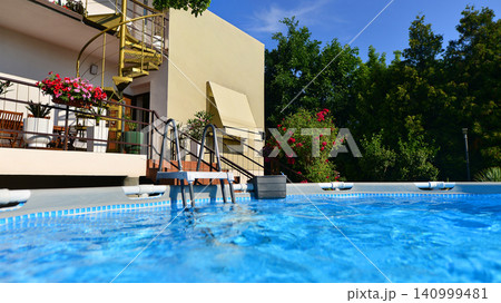 Large swimming pool set in the backyard next to the house. Large swimming pool set in the backyard next to the house. 140999481