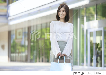 ショッピングバックを持って立つ笑顔の30代女性 屋外のライフスタイル ショッピングバックを持って立つ笑顔の30代女性 屋外のライフスタイル 141000672