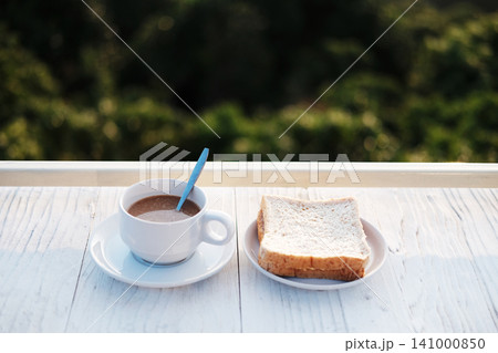 A cup of hot coffee with toast bread in white dish on white wooden counter bar is breakfast in resort on the mountain in Thailand 141000850