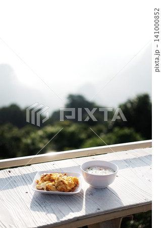 Rice soup and omelet in white plate on white wooden counter bar outdoor is breakfast in resort on the mountain in Thailand Rice soup and omelet in white plate on white wooden counter bar outdoor is breakfast in resort on the mountain in Thailand 141000852