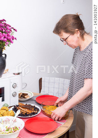 A woman sets plates on a table for breakfast. She arranges food like pie and pancakes, salad, and other dishes in a casual dining area during the morning hours A woman sets plates on a table for breakfast. She arranges food like pie and pancakes, salad, and other dishes in a casual dining area during the morning hours 141001927