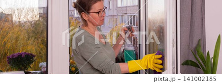 A person is cleaning the windows of an apartment balcony in the fall season. Flowers are present in pots, and the sun is shining on the scene, banner A person is cleaning the windows of an apartment balcony in the fall season. Flowers are present in pots, and the sun is shining on the scene, banner 141002185