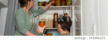 A married couple is busy placing canned goods on shelves in their pantry. They are in their city home, preparing for autumn. Boxes are organized, and the couple works together, banner A married couple is busy placing canned goods on shelves in their pantry. They are in their city home, preparing for autumn. Boxes are organized, and the couple works together, banner 141002225