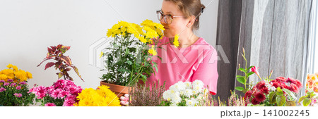Woman 50 years old transplanting autumn flowers chrysanthemums and heathers into pots and holding a pot with a chrysanthemum and smiling, decorating a home terrace or balcony with flowers, banner Woman 50 years old transplanting autumn flowers chrysanthemums and heathers into pots and holding a pot with a chrysanthemum and smiling, decorating a home terrace or balcony with flowers, banner 141002245