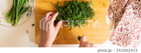 A person is chopping herbs on a wooden board while other fresh vegetables are arranged on a table. Bowls of diced tomatoes and salad dressing are also present, banner A person is chopping herbs on a wooden board while other fresh vegetables are arranged on a table. Bowls of diced tomatoes and salad dressing are also present, banner 141002433