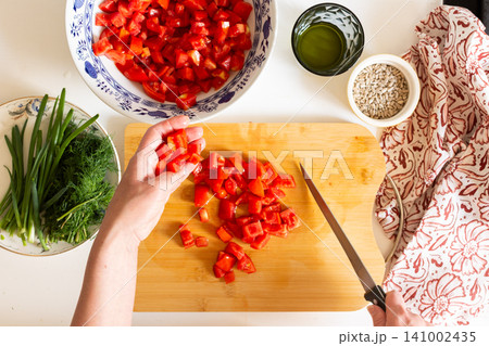 A person is chopping fresh tomatoes on a wooden board to prepare a salad. Nearby are bowls of other chopped vegetables and ingredients, all from local sources, showing a summer harvest A person is chopping fresh tomatoes on a wooden board to prepare a salad. Nearby are bowls of other chopped vegetables and ingredients, all from local sources, showing a summer harvest 141002435