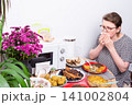 A person sits at a kitchen table eating food. Dishes with different homemade meals are arranged around her. Flowers add color to the table setting. A microwave is nearby 141002804
