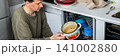 A man is putting dirty dishes into the dishwasher in his kitchen. He focuses on the task while several items rest in the appliance, ready for cleaning, banner 141002880