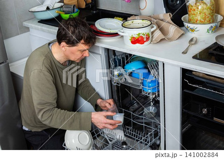A man is at work in the kitchen, pouring salt into a dishwasher as he prepares to wash dirty dishes. He is focused on the task at hand while organizing the appliances A man is at work in the kitchen, pouring salt into a dishwasher as he prepares to wash dirty dishes. He is focused on the task at hand while organizing the appliances 141002884
