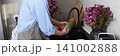 A man stands at the sink in his kitchen, cleaning dirty dishes and utensils. Flowers are placed on the counter, adding color to the scene in daylight, banner 141002888