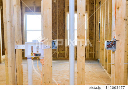 Workers are installing plumbing pipes electrical boxes in framework of house during building process. 141003477