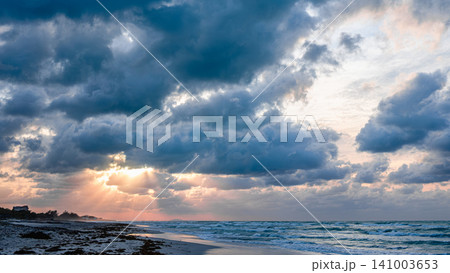 Beautiful sunset over the beach with dramatic clouds and shimmering ocean waves Beautiful sunset over the beach with dramatic clouds and shimmering ocean waves 141003653