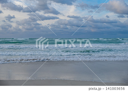 Waves crash on the shore under a cloudy sky at twilight on a beach 141003656