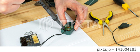 A man is using a tool to fix the wiring of a Christmas tree garland. Tools are spread out on the table as he works carefully in a room decorated for the holidays, banner A man is using a tool to fix the wiring of a Christmas tree garland. Tools are spread out on the table as he works carefully in a room decorated for the holidays, banner 141004183