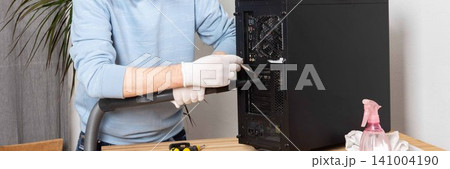 A 53-year-old man removes dust from a computer system unit using a brush while wearing gloves. He is focused on maintaining the computer in a room with plants A 53-year-old man removes dust from a computer system unit using a brush while wearing gloves. He is focused on maintaining the computer in a room with plants 141004190