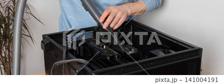 A 53-year-old man uses a vacuum attachment to remove dust from a computer system unit in a home office. The room is well lit and organized for the task, banner A 53-year-old man uses a vacuum attachment to remove dust from a computer system unit in a home office. The room is well lit and organized for the task, banner 141004191