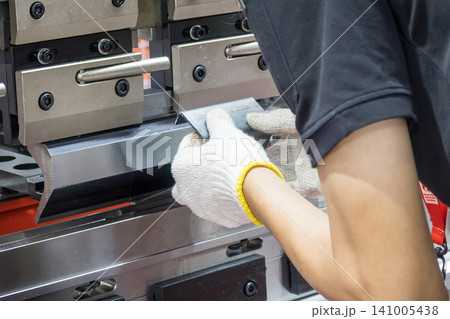 Industrial metalworker holding a sheet metal part into a press brake bending machine. 141005438