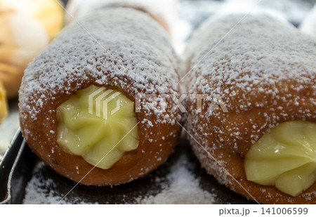 Naples, italy. December 27, 2024. Sweet neapolitan bomboloni donut, a traditional dessert, topped with powdered sugar and filled with yellow cream 141006599