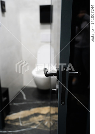 Modern public restroom entrance with glass door leading into clean bathroom interior. Sanitation hygiene and public facility design 141007244