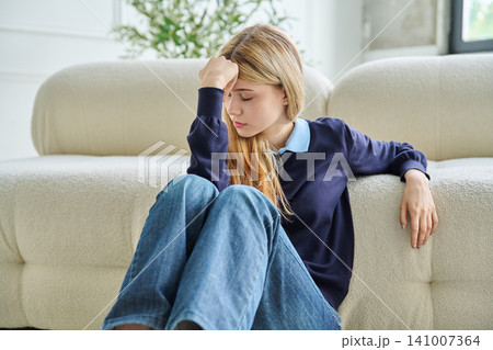 Tired teenage student girl with headache sitting on floor holding forehead. 141007364